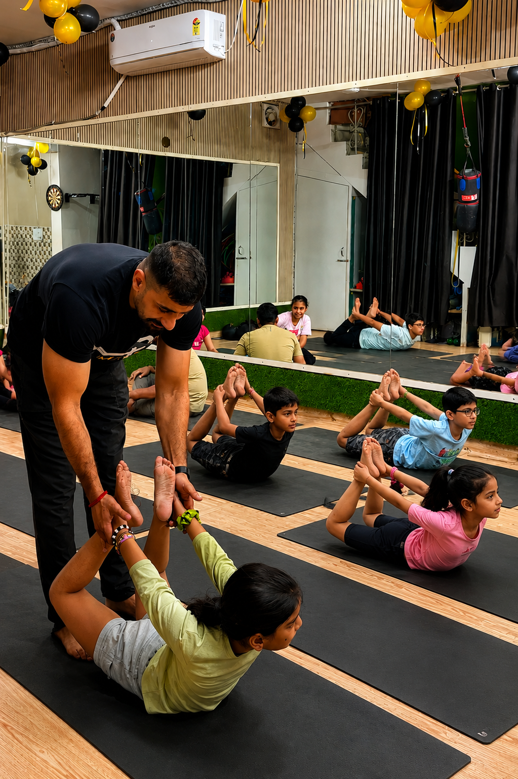 Sudhir guiding a young student into bow pose during a kids' class